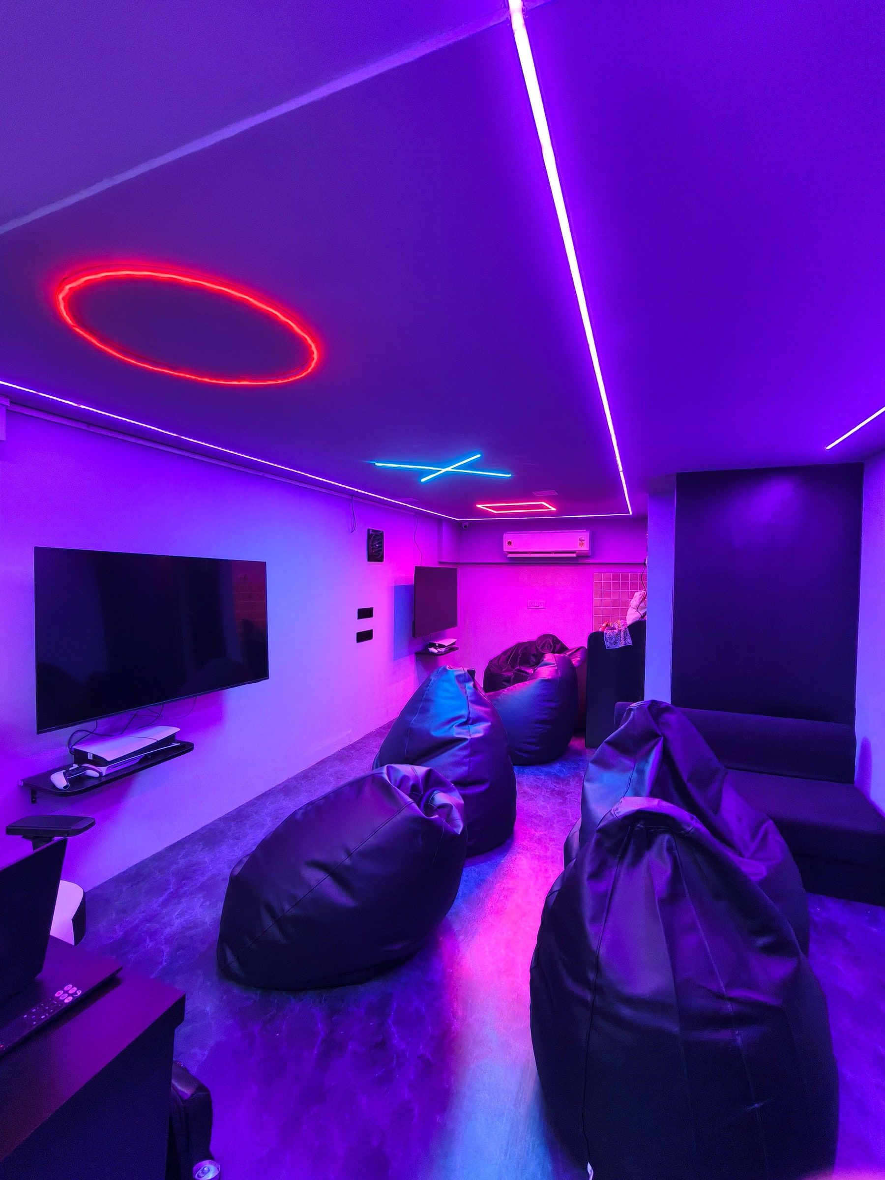 The PS5 lounge: a wall-mounted TV with a PS5 and controllers, bean bags and neon lights on the ceiling.