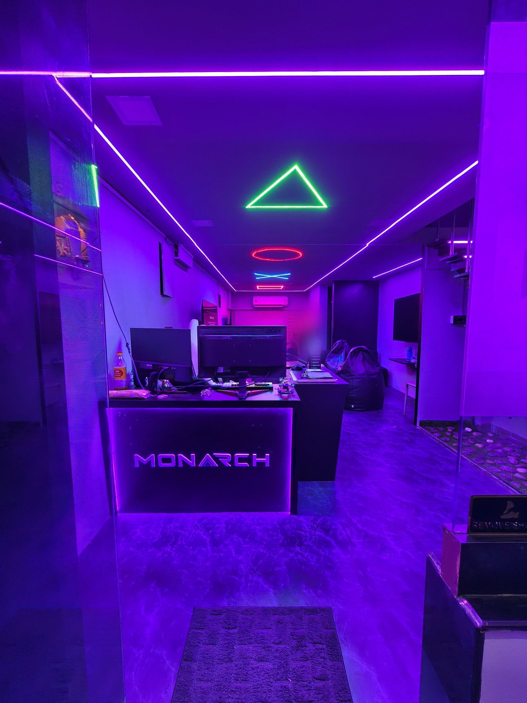 Monarch's ground-floor reception: the lit MONARCH desk at the entrance, neon shapes on the ceiling and the lounge beyond.
